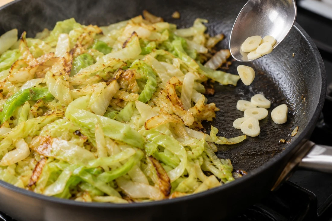 Sliced garlic added beside cabbage in a skillet Sliced garlic added beside cabbage in a skillet