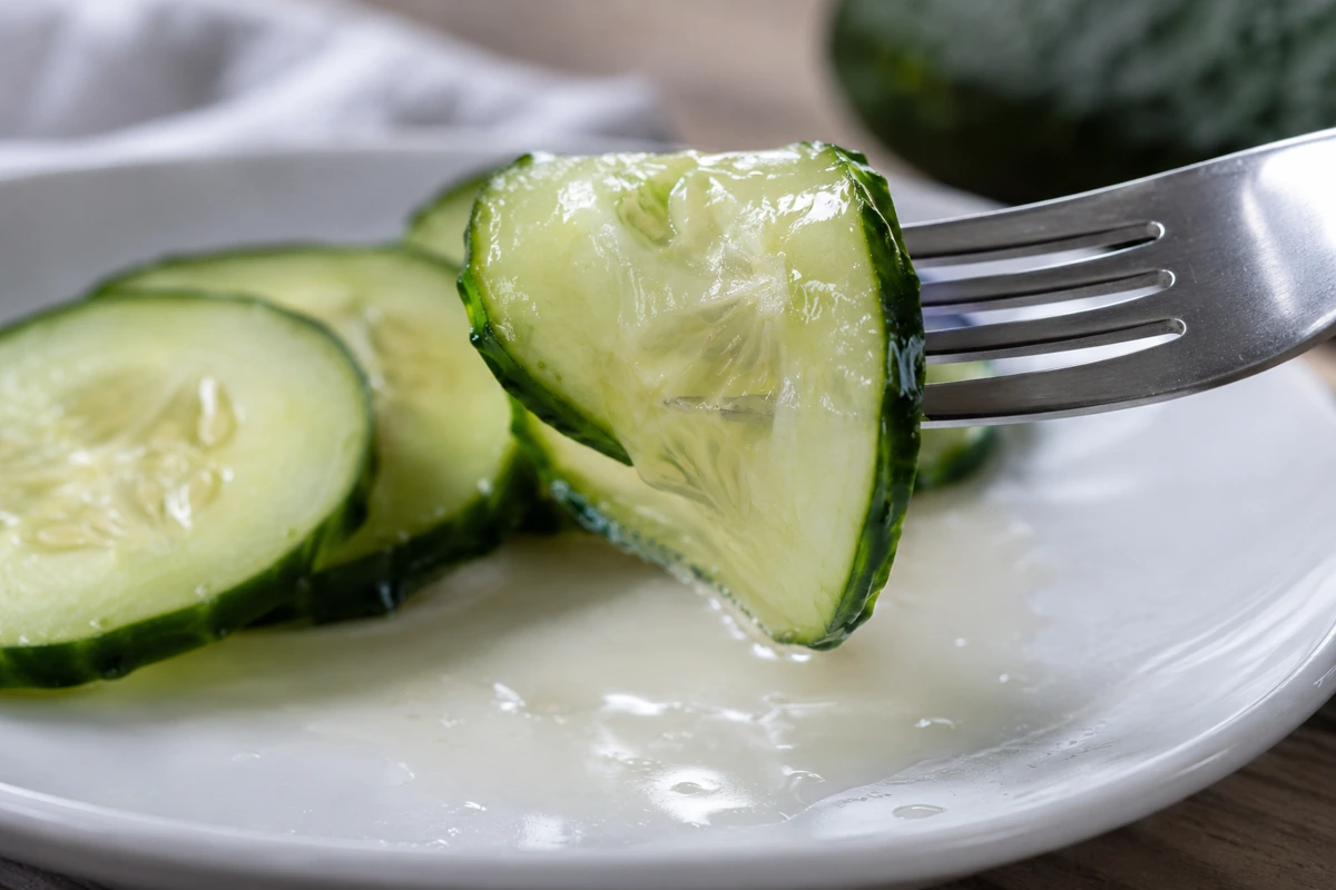 Soft cucumber round bending over a fork above released liquid Soft cucumber round bending over a fork above released liquid
