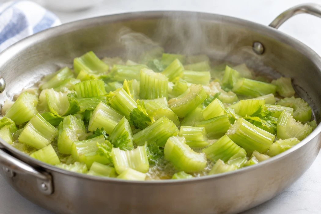 Celery pieces cooking in a shallow pan with visible steam Celery pieces cooking in a shallow pan with visible steam