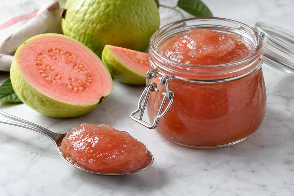 Smooth seedless guava jam on a spoon beside an open jar