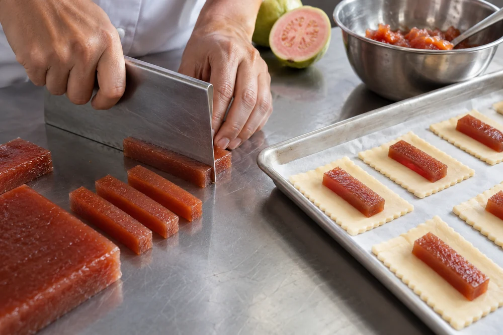 Guava paste cut into fingers beside unbaked pastry squares Guava paste cut into fingers beside unbaked pastry squares
