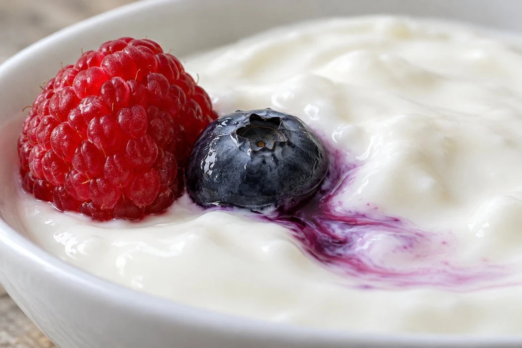 Blueberry and raspberry touching white yogurt with a purple color trail