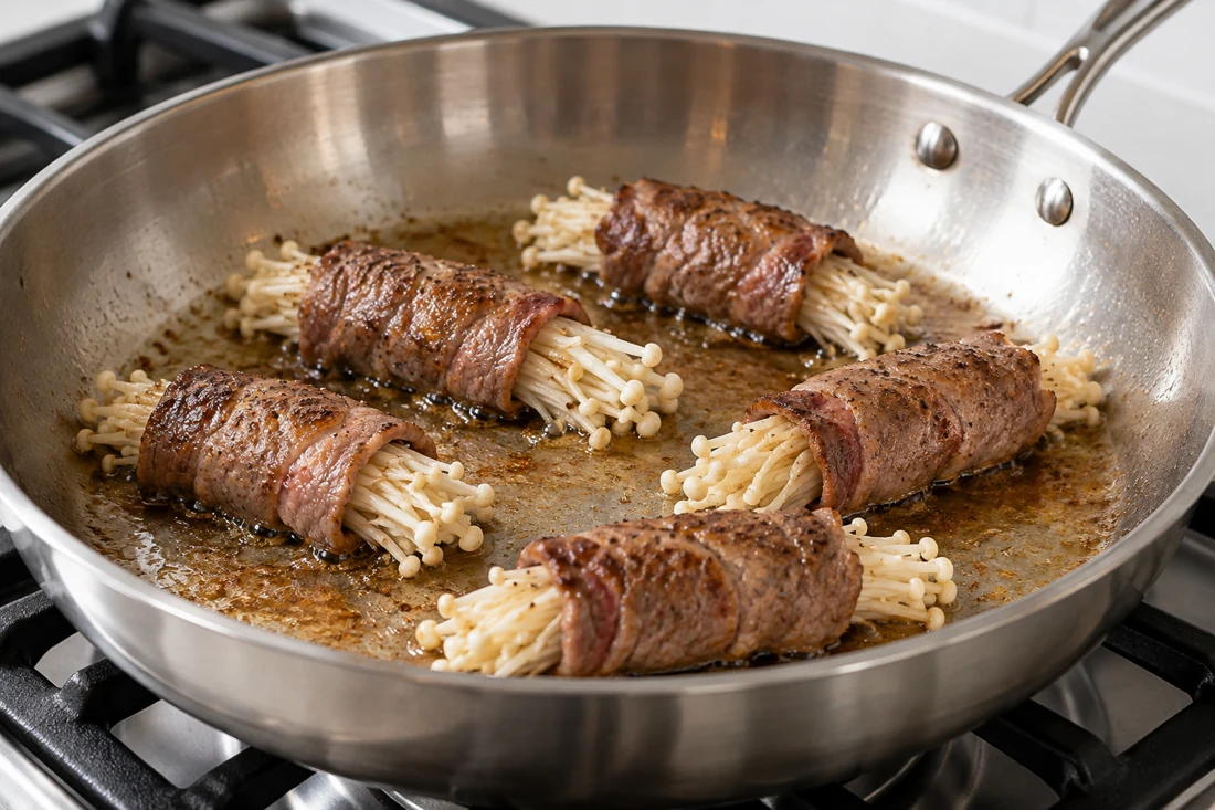 Spaced beef enoki rolls browning in a shallow pan Spaced beef enoki rolls browning in a shallow pan