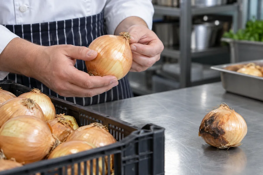 Cook checks a whole onion while a visibly decayed onion is separated