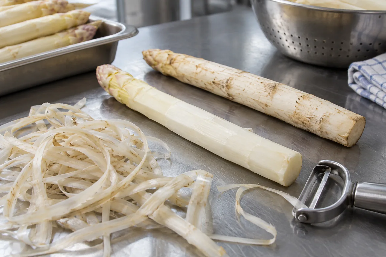 White asparagus spear beside removed outer peel and an unpeeled spear.