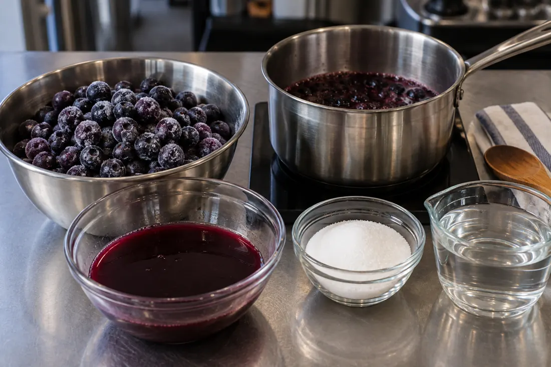 Blueberries, thaw juice, sugar and water beside a small kettle